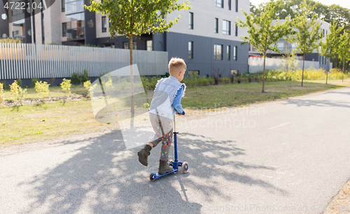 Image of happy little boy riding scooter in city