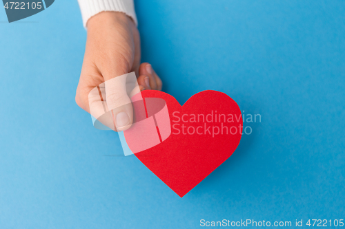 Image of hand holding red heart shape on blue background