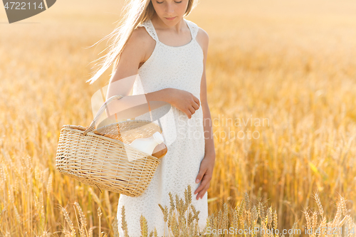 Image of girl with bread and milk in basket on cereal field