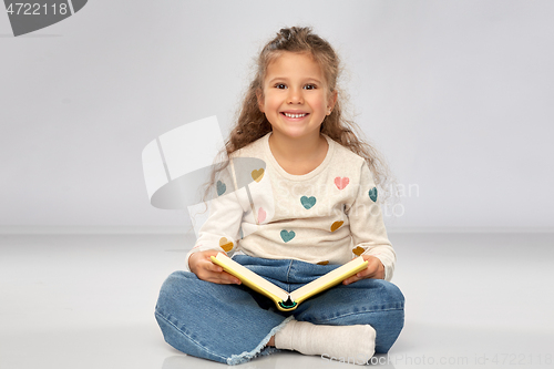 Image of beautiful smiling girl reading book on floor