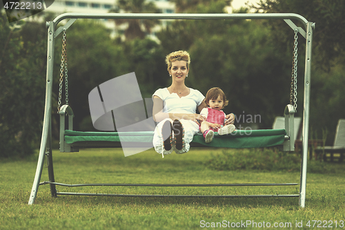 Image of mother and little daughter swinging at backyard