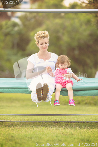 Image of mother and little daughter swinging at backyard