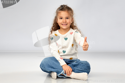 Image of little girl sitting on floor and showing thumbs up