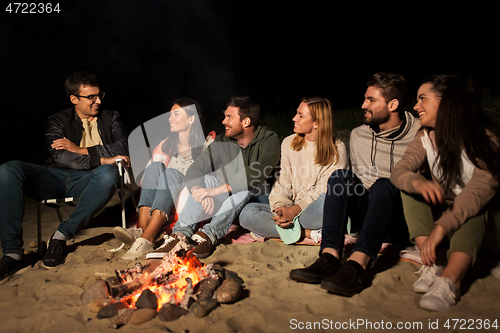 Image of group of friends sitting at camp fire on beach