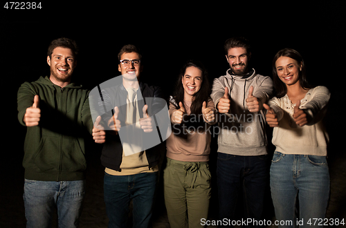 Image of happy smiling friends showing thumbs up at night