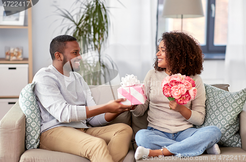 Image of happy couple with flowers and gift at home