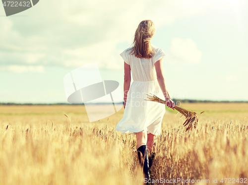 Image of young woman with cereal spikelets walking on field