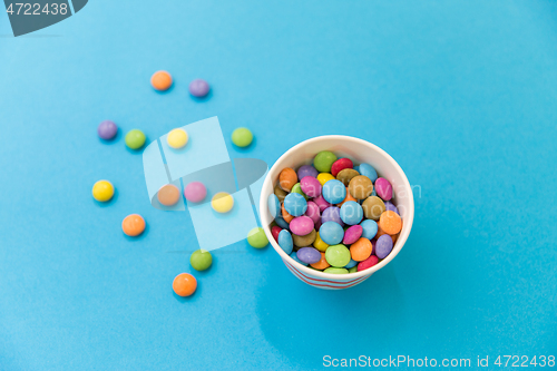 Image of candy drops in paper cup on blue background