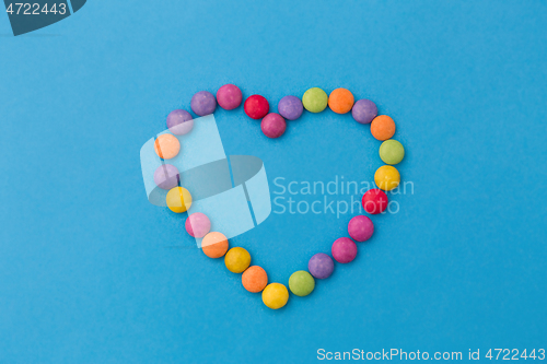 Image of candy drops in shape of heart on blue background