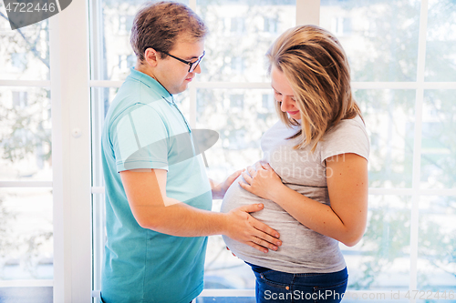 Image of Beautiful pregnant woman and man sitting near wall