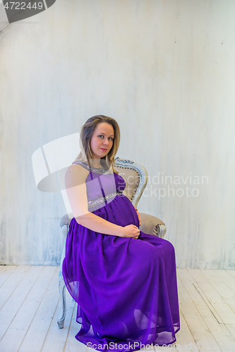 Image of Beautiful pregnant woman in ultra violet dress sitting on the armchair