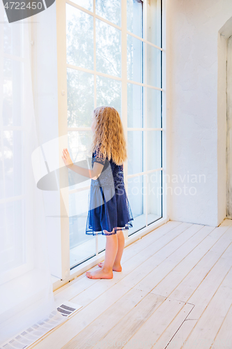 Image of Cute girl in casual clothes standing near the window and watching out