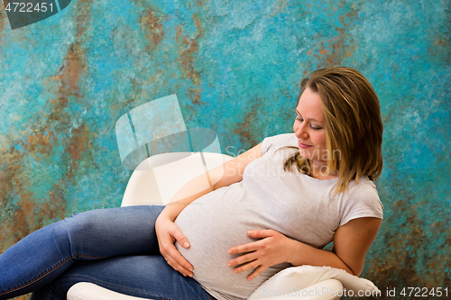 Image of Young pregnant woman sitting on the armchair