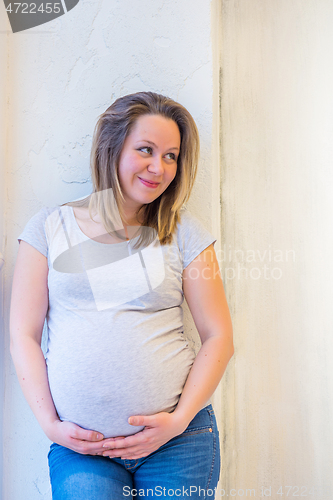 Image of Beautiful pregnant woman standing near window at home in light interior