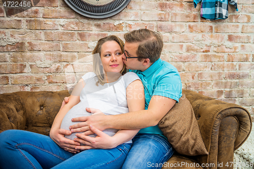 Image of A man kissing his pregnant woman. A man kissing his pregnant woman. They are sitting.