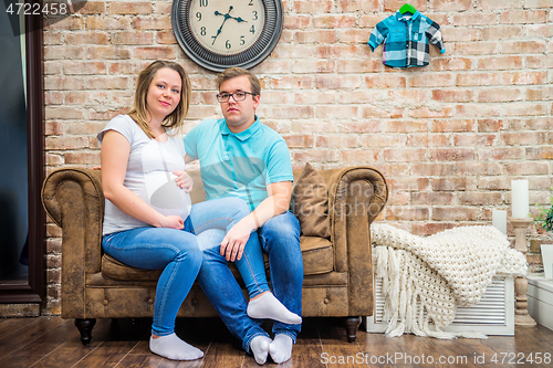 Image of Beautiful pregnant woman and man sitting near wall