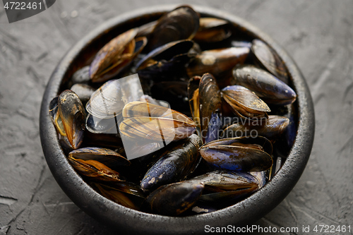 Image of Fresh and raw sea mussels in black ceramic bowl placed on dark stone background