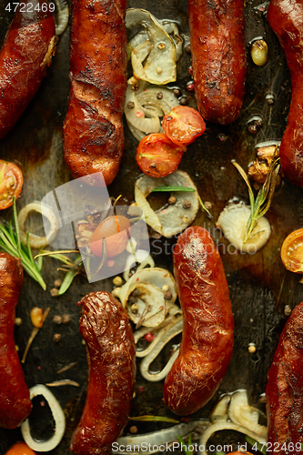 Image of Tasty grilled homemade rosemary sausages placed on iron frying tray over rustic dark stone table