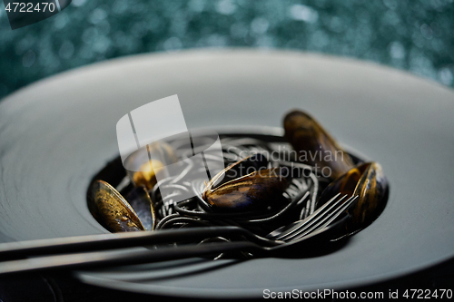 Image of Seafood black spaghetti pasta with clams served on black plate on dark stone