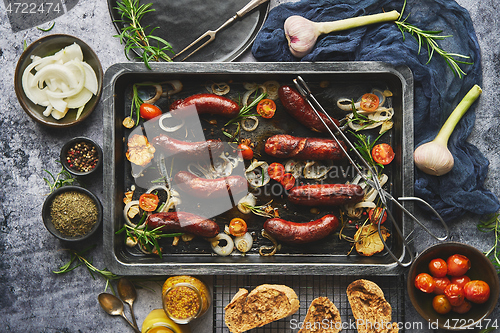 Image of Top view on delicious grilled sausages served with onion, tomatoes, garlic, bread and herbs