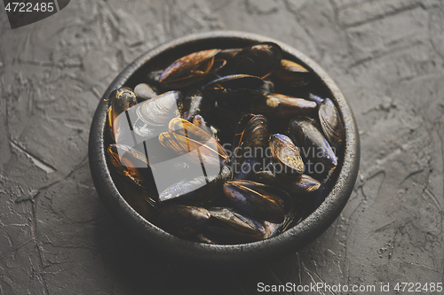 Image of Fresh and raw sea mussels in black ceramic bowl placed on dark s