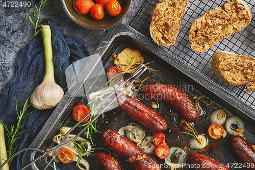 Image of Tasty grilled homemade rosemary sausages placed on iron frying tray over rustic dark stone table