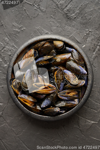 Image of Fresh and raw sea mussels in black ceramic bowl placed on dark stone background