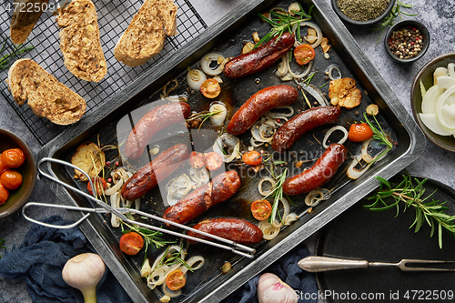 Image of Top view on delicious grilled sausages served with onion, tomatoes, garlic, bread and herbs