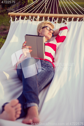 Image of woman using a tablet computer while relaxing on hammock