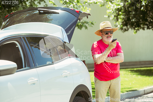 Image of Senior man standing near by his car is working outdoors