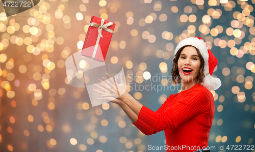 Image of happy young woman in santa hat catching gift box
