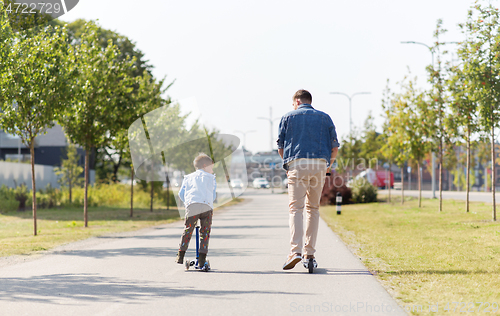 Image of happy father and little son riding scooter in city