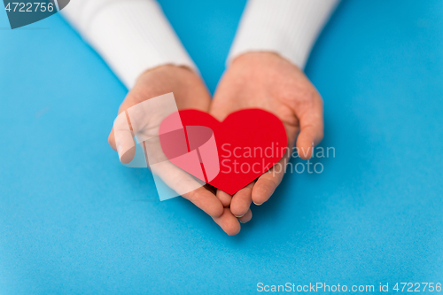 Image of hands holding red heart shape on blue background