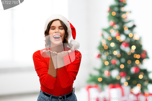 Image of happy young woman in santa hat sending air kiss