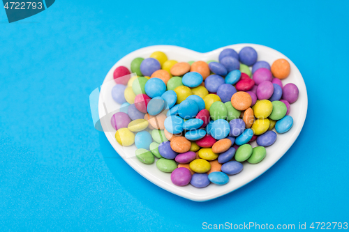 Image of candies on heart shaped plate over blue background