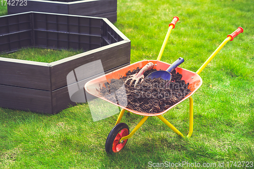 Image of Garden barrow with soil and empty raised beds on grass prepared for filling with soil