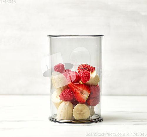 Image of fresh banana pieces and red berries in plastic transparent blend