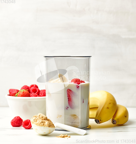 Image of fresh banana, berries and milk in blender container 