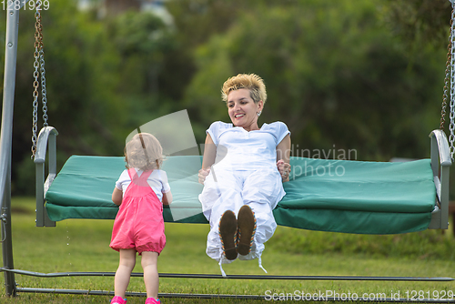 Image of mother and little daughter swinging at backyard