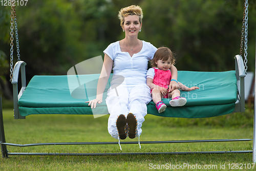 Image of mother and little daughter swinging at backyard