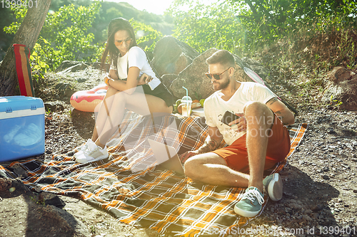 Image of Young couple having picnic at riverside in sunny day