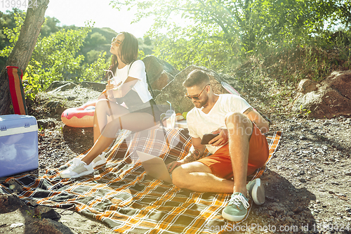 Image of Young couple having picnic at riverside in sunny day