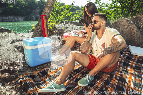 Image of Young couple having picnic at riverside in sunny day