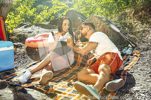 Image of Young couple having picnic at riverside in sunny day