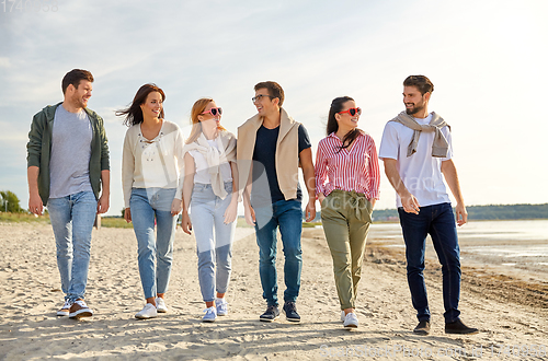 Image of happy friends walking along summer beach