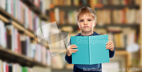 Image of displeased little boy reading book over library