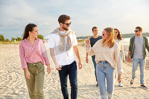 Image of happy friends walking along summer beach