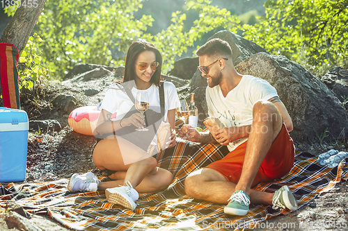 Image of Young couple having picnic at riverside in sunny day