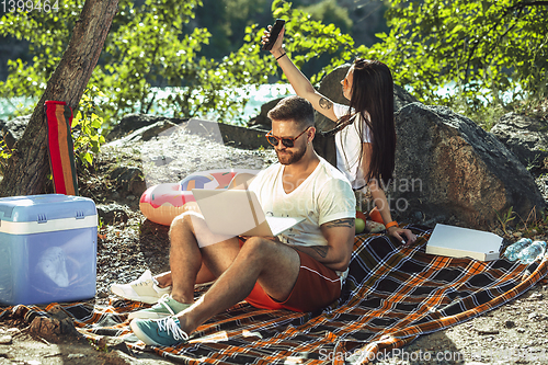 Image of Young couple having picnic at riverside in sunny day