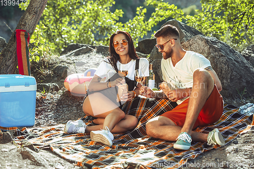 Image of Young couple having picnic at riverside in sunny day